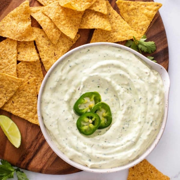 Bowl of jalapeño dip garnished with sliced jalapeños next to tortilla chips.