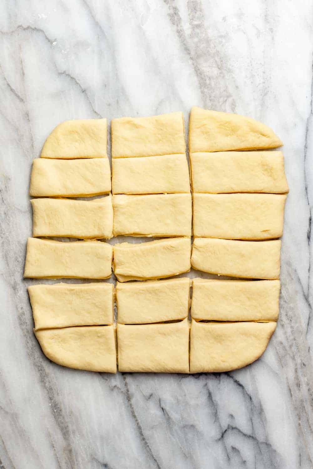 Dough rolled out on a marble surface and cut into pieces to make parker house rolls