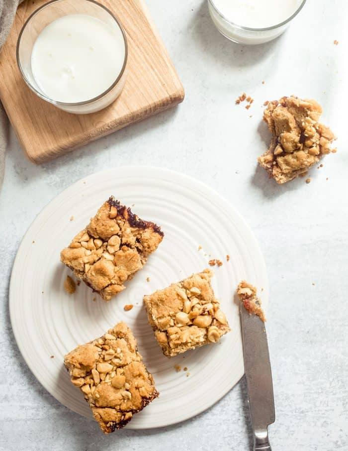 Overhead view of three peanut butter and jelly bars on a white plate next to a glass of milk