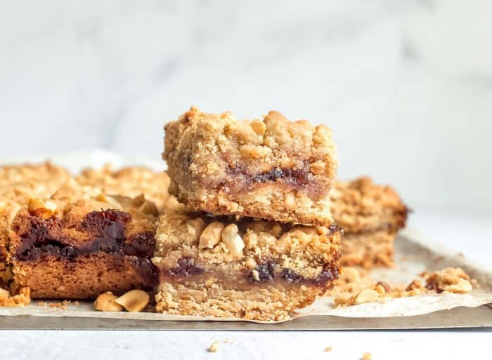 Peanut butter and jelly bars stacked on a parchment-lined tray