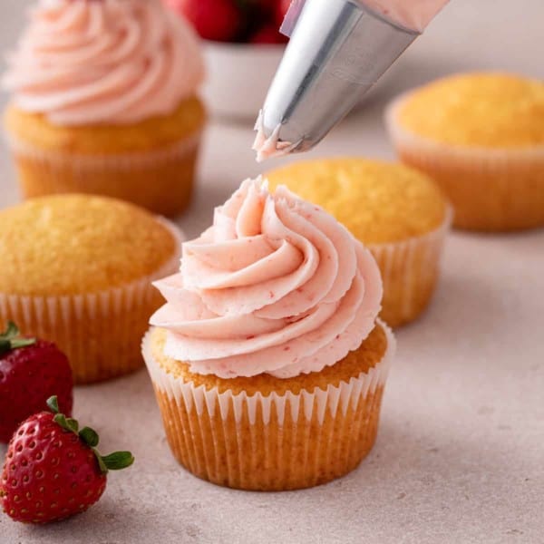 Strawberry frosting being piped onto a cupcake.