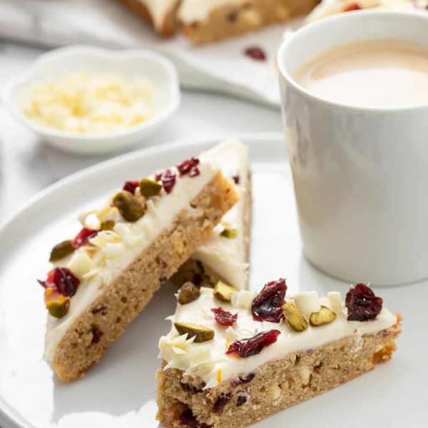 Three cranberry bliss bars arranged on a white plate, with a bite taken out of one of them