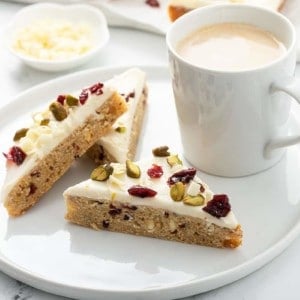 Three cranberry bliss bars set next to a cup of coffee on a white plate