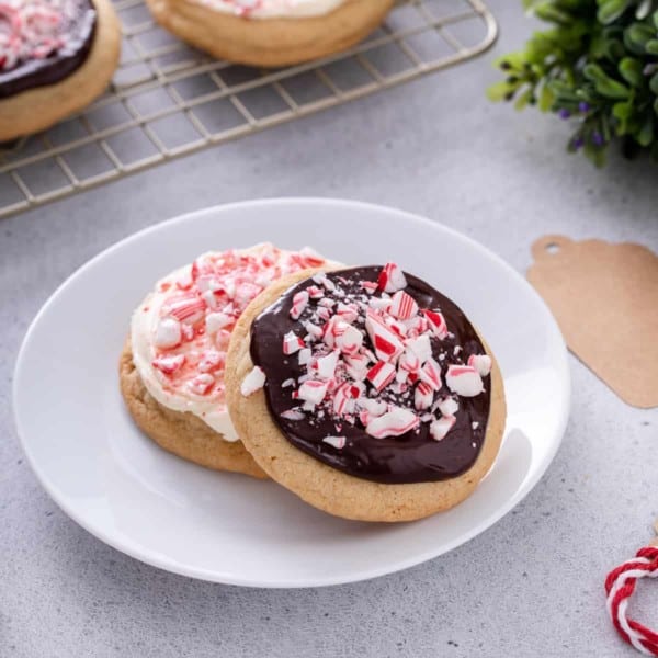 Two peppermint cookies – one topped with cream cheese frosting and one topped with chocolate ganache – on a white plate.