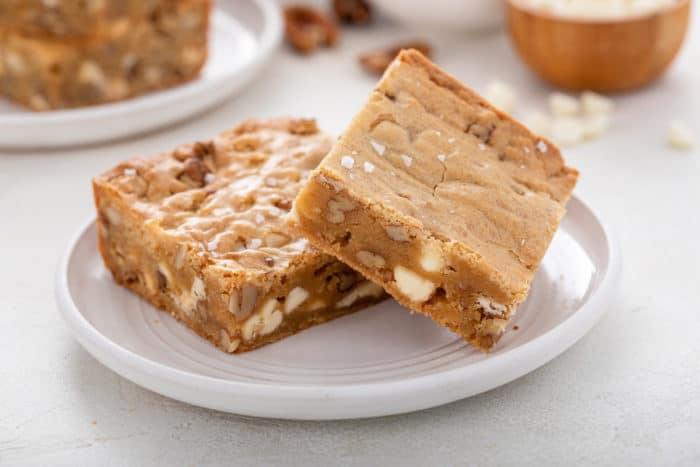 Two white chocolate pecan blondies on a white plate.