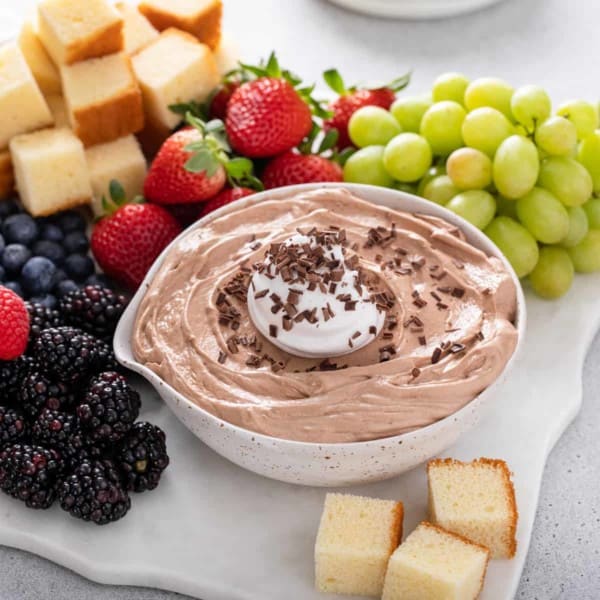 Bowl of nutella fruit dip on a platter with fresh fruit and cubes of pound cake.