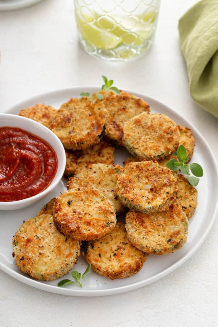 White plate filled with air fryer zucchini chips and a small bowl of marinara sauce.