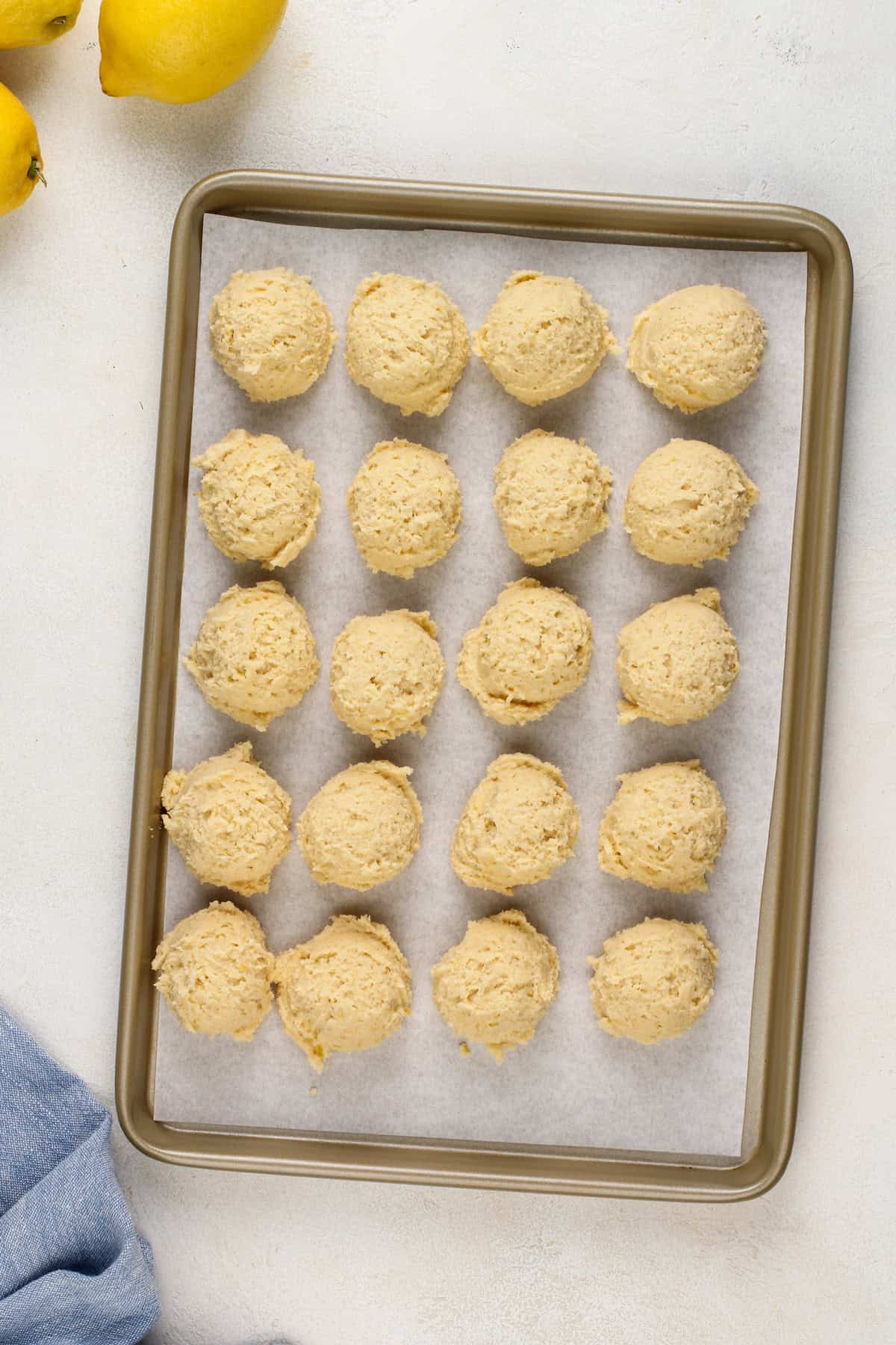 Balls of lemon cookie dough lined up on a baking sheet to go in the freezer.