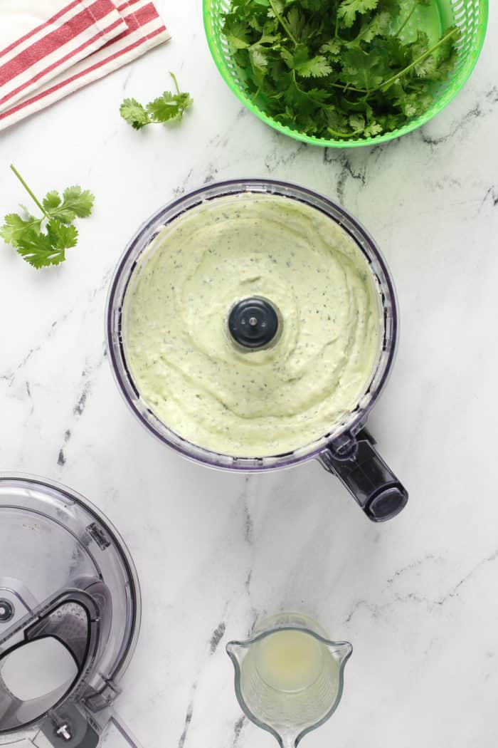 Processed jalapeño dip in the bowl of a food processor on a marble countertop.