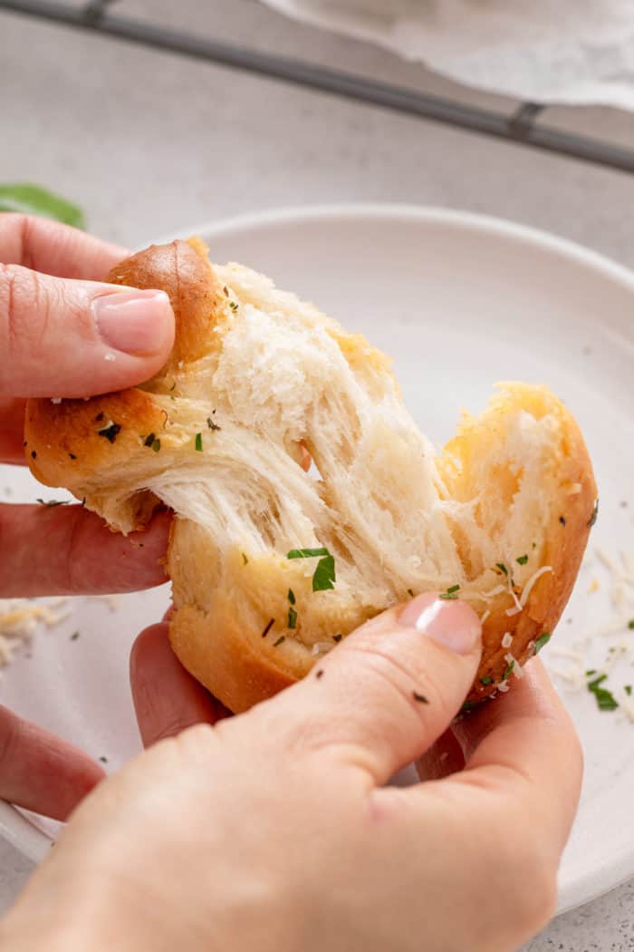 Hands pulling apart a garlic knot to show the soft texture inside.