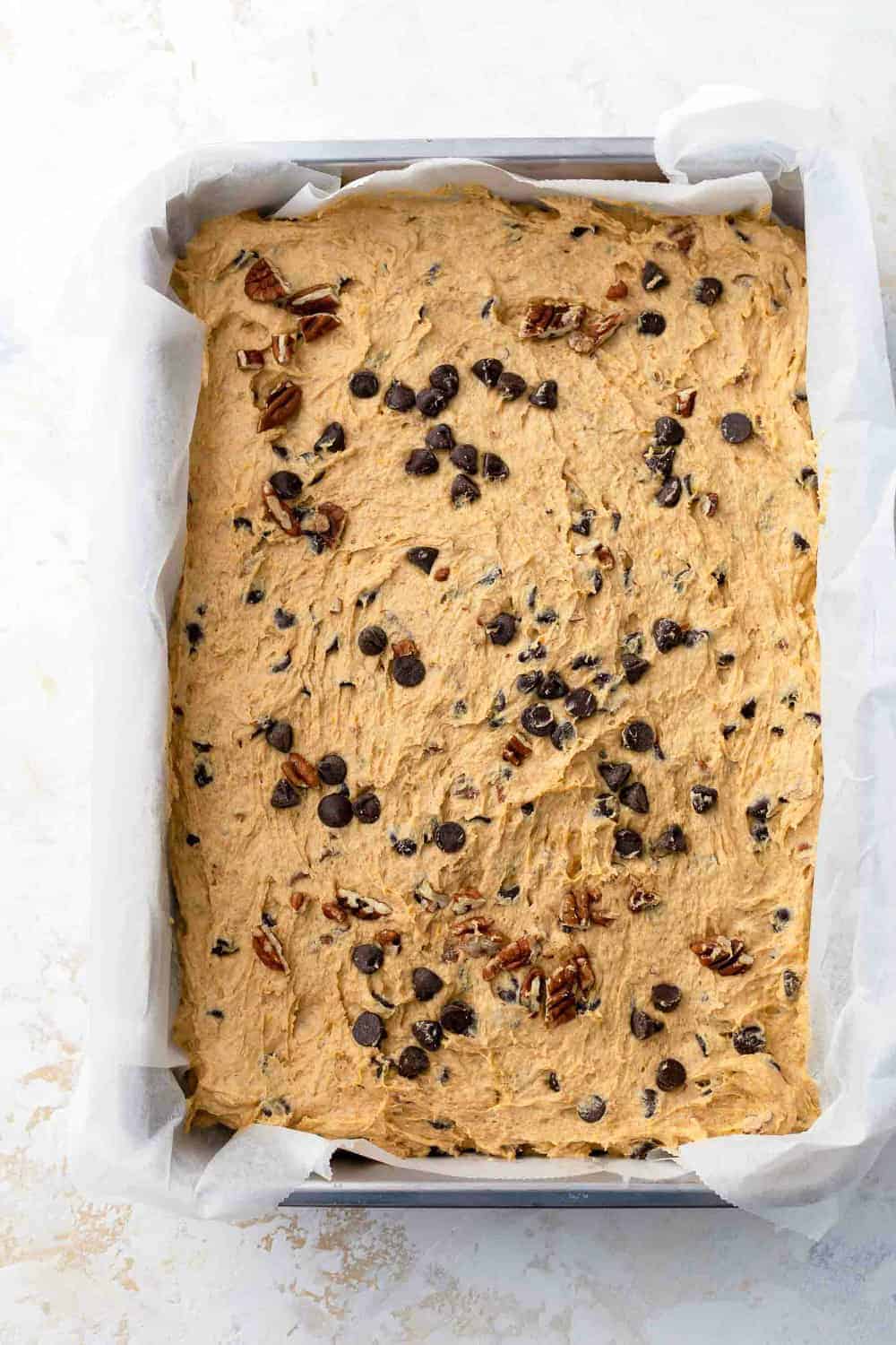 Pumpkin blondie batter in a parchment-lined pan, ready to bake