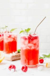 Glass of raspberry lemonade with a sprig of mint and a metal straw in the foreground, with 2 more glasses of lemonade in the background