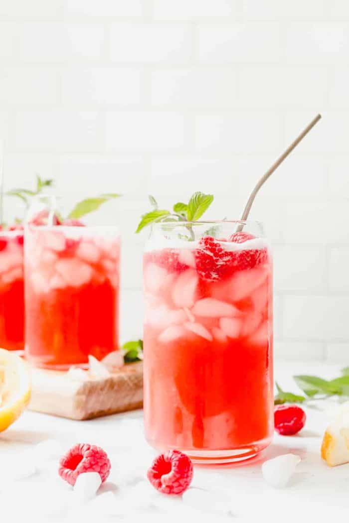 Glass of raspberry lemonade with a sprig of mint and a metal straw in the foreground, with 2 more glasses of lemonade in the background