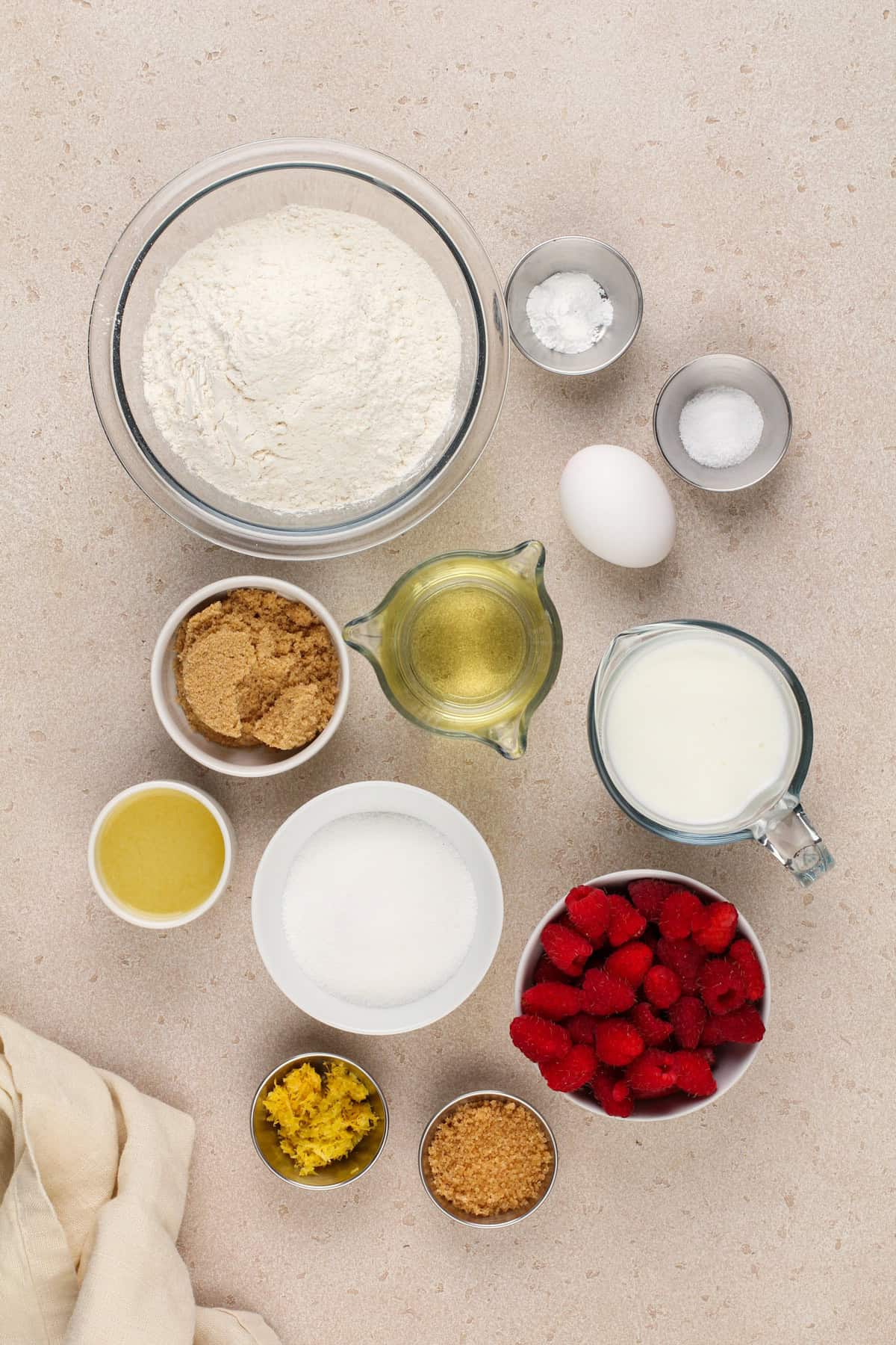 Ingredients for lemon raspberry muffins arranged on a beige countertop.