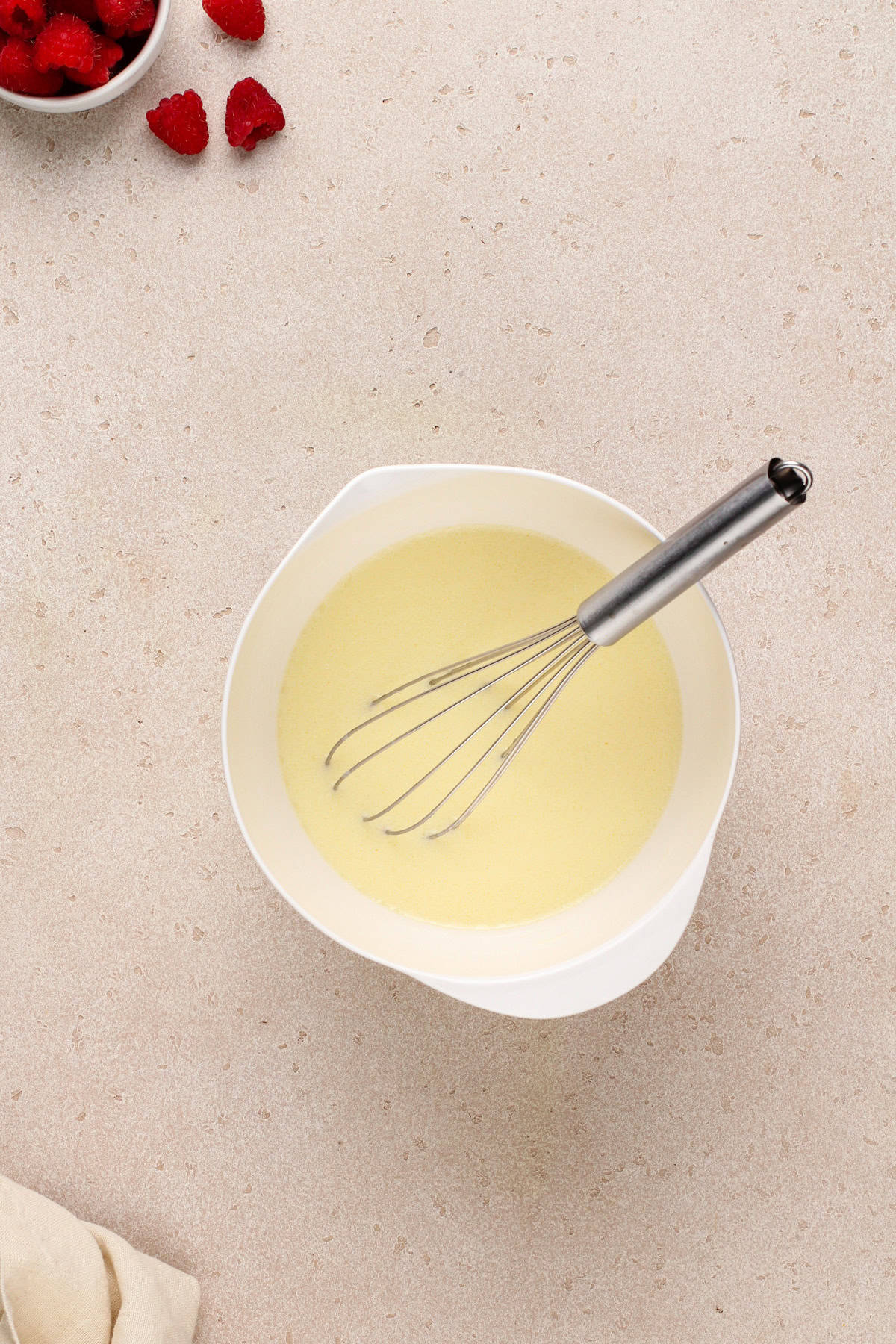 Wet ingredients for lemon raspberry muffins in a white bowl.