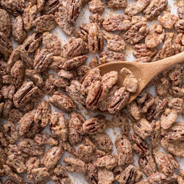 Candied pecans on a baking sheet being stirred with a wooden spoon.