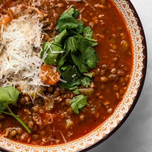 Close up of a bowl of sausage and lentil soup garnished with herbs and parmesan cheese