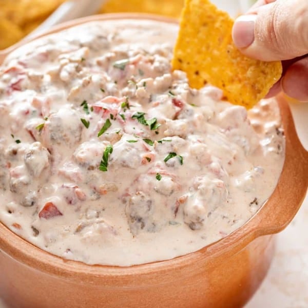 Hand scooping up spicy sausage dip with a tortilla chip