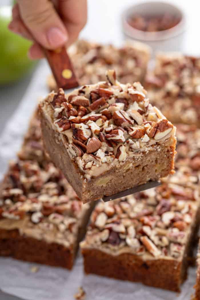 Cake server lifting a caramel apple blondie up from a piece of parchment paper.