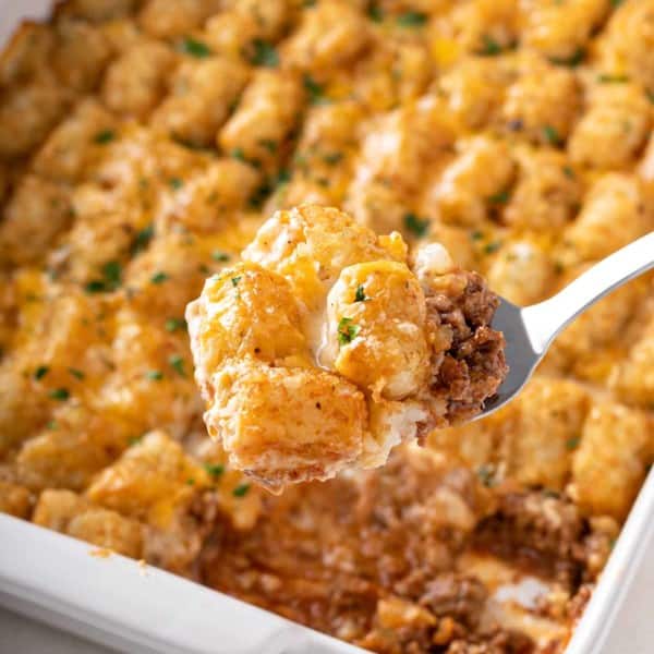 Spoon scooping a serving of cheeseburger tater tot casserole out of the baking dish