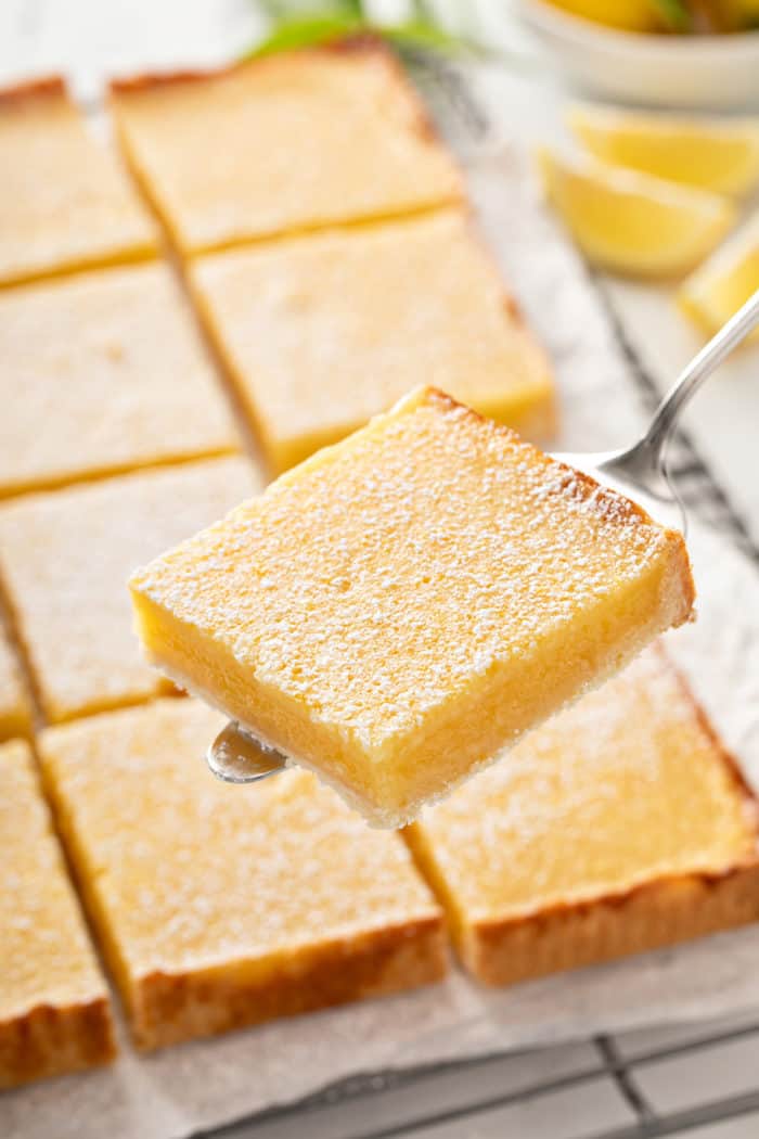 Pie server holding up a sliced lemon bar.