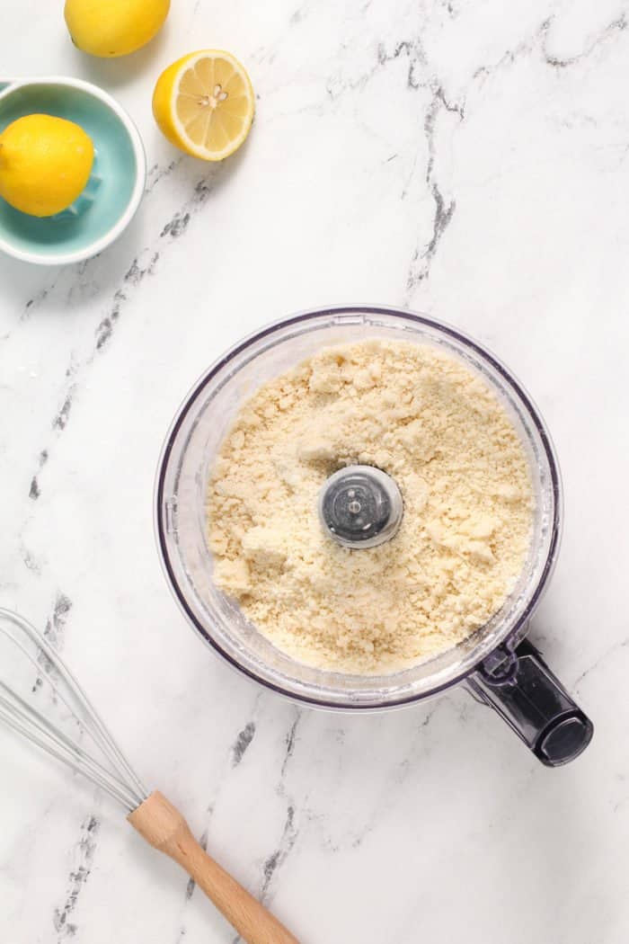 Shortbread crust pulsed in a food processor bowl set on a marble countertop.