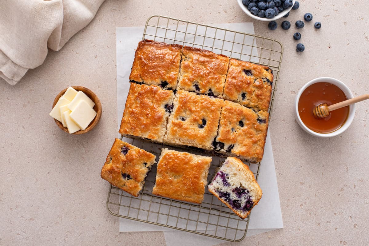 Overhhead view of a sliced pan of blueberry biscuits on a wire rack.