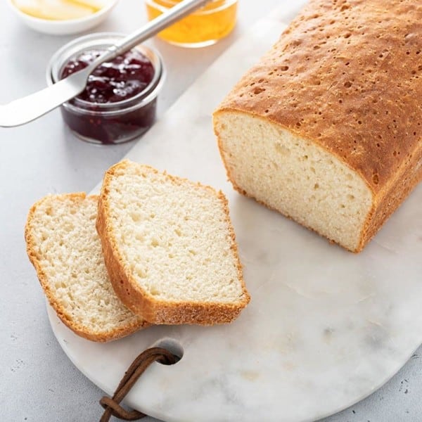 Sliced loaf of English muffin bread set on a marble board next to a bowl of jam