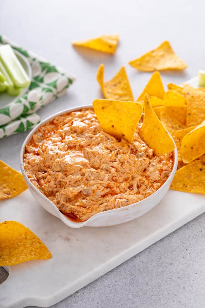 White bowl of slow cooker buffalo chicken dip with two tortilla chips in it.