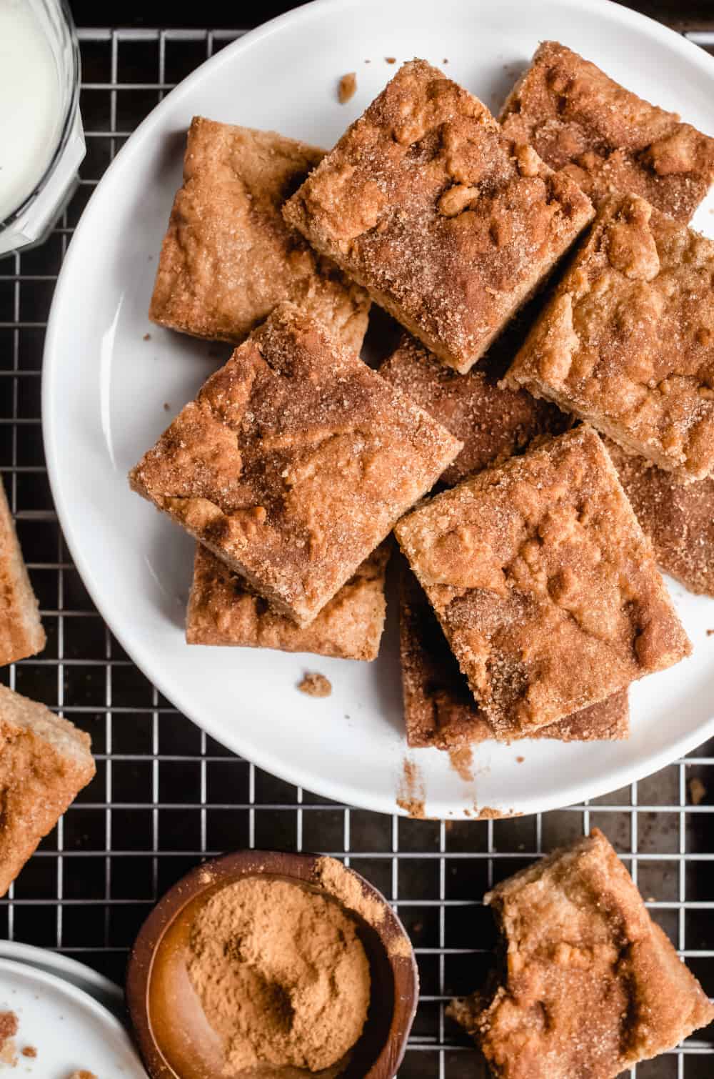 Cut snickerdoodle blondies arranged on a white plate that is set on a wire rack