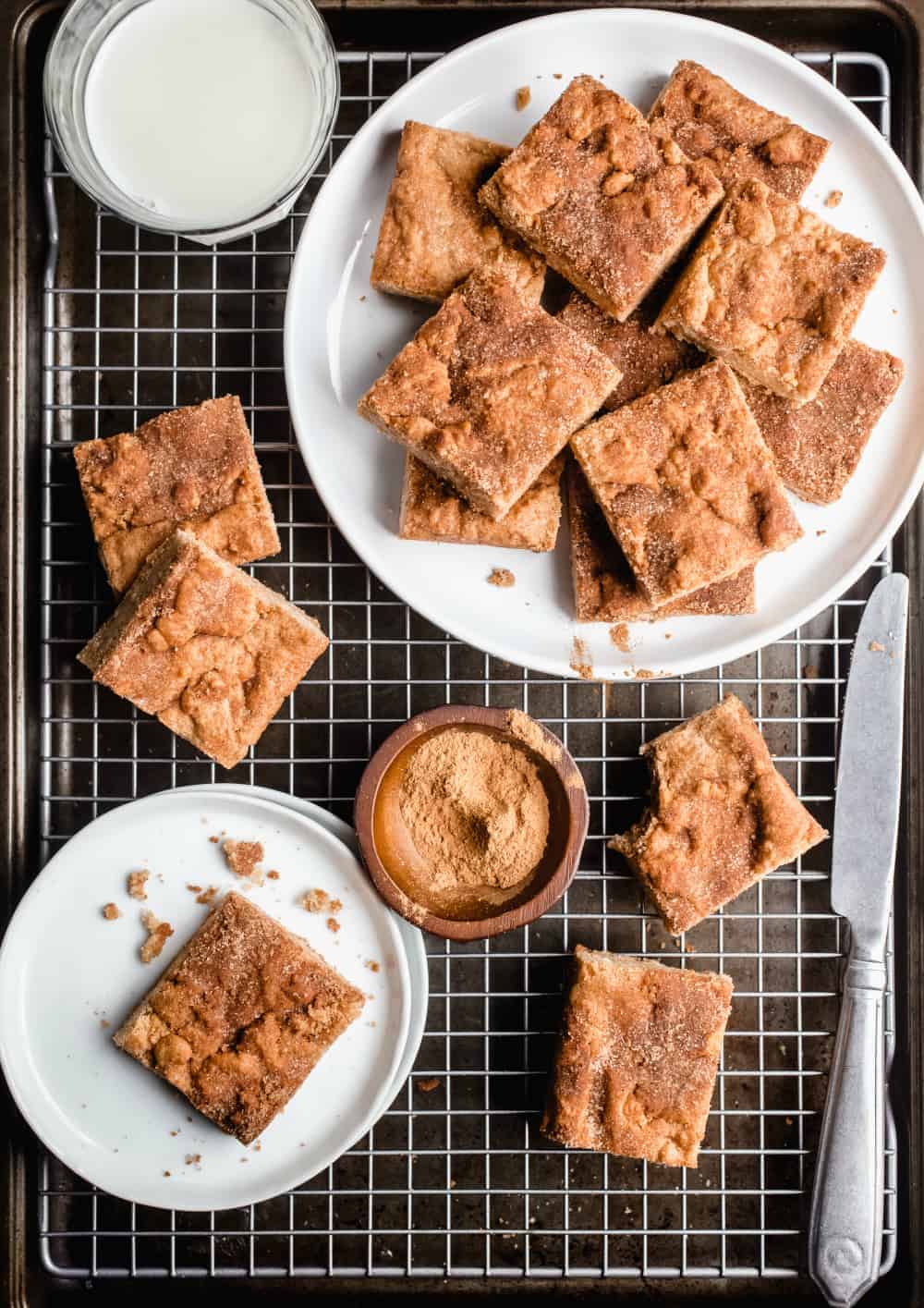 White plate filled with snickerdoodle blondies on top of a wire rack alongside several scattered blondies