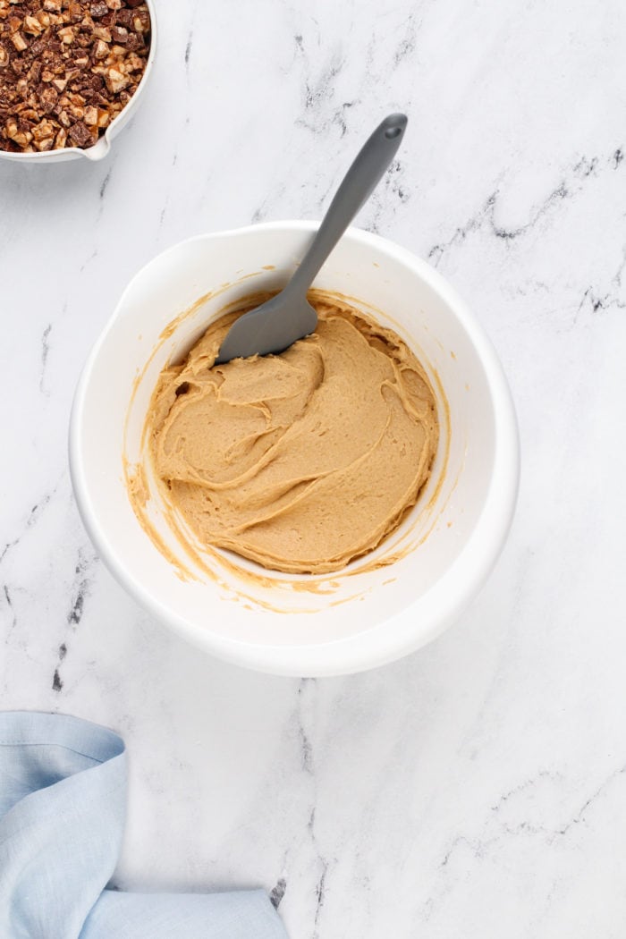 Peanut butter and cream cheese base for snickers dip mixed in a white mixing bowl.