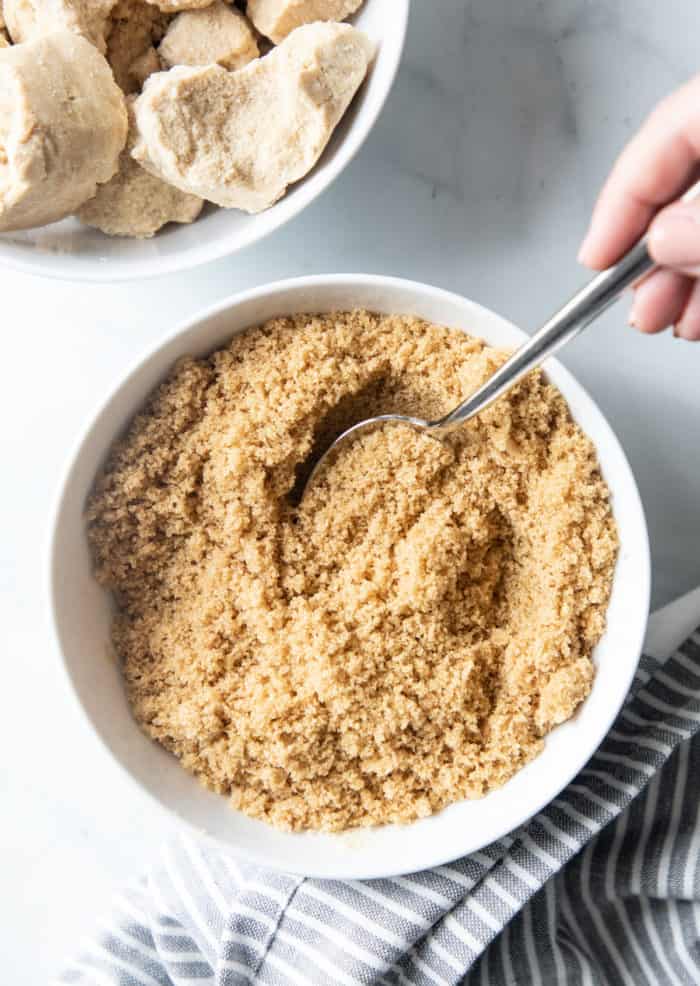 Hand stirring soft brown sugar in a white bowl with a fork.