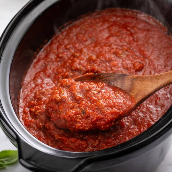 Wooden spoon holding spaghetti sauce over a crockpot.