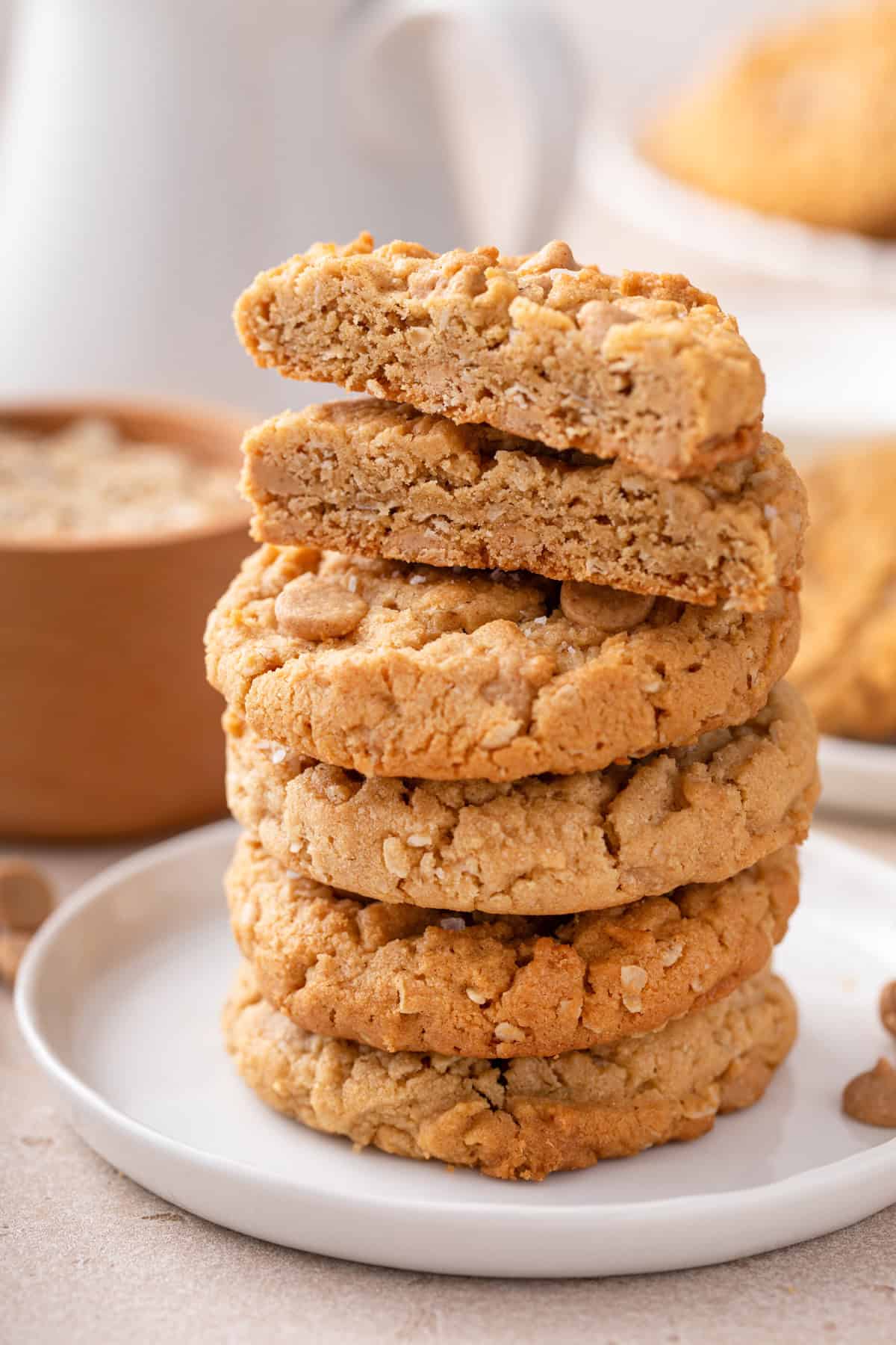 Stack of peanut butter oatmeal cookies on a white plate. The top cookie is cut in half to show the inside texture.