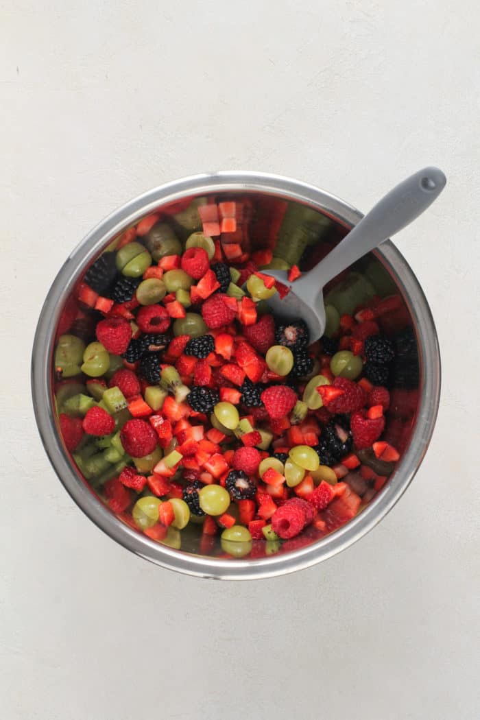 Spatula stirring diced fresh fruit in a metal bowl.