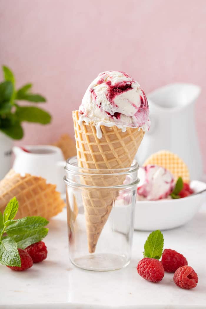 Scoop of vanilla ice cream in a waffle cone. The cone is propped up in a glass jar.