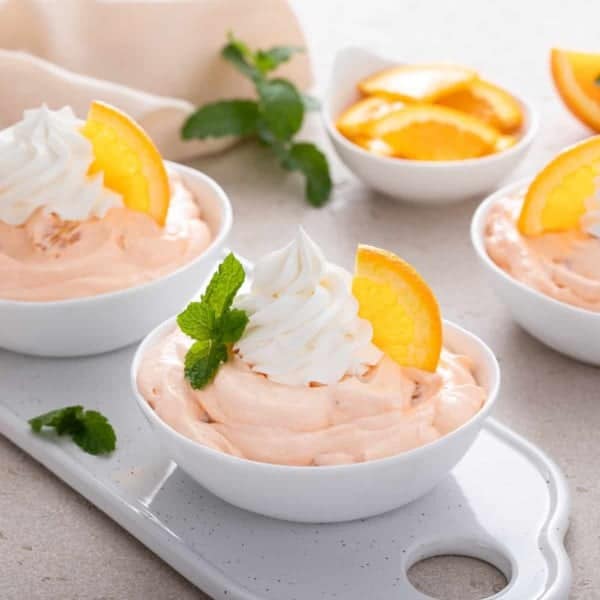 Bowls filled with orange fluff and garnished with whipped cream and orange slices.