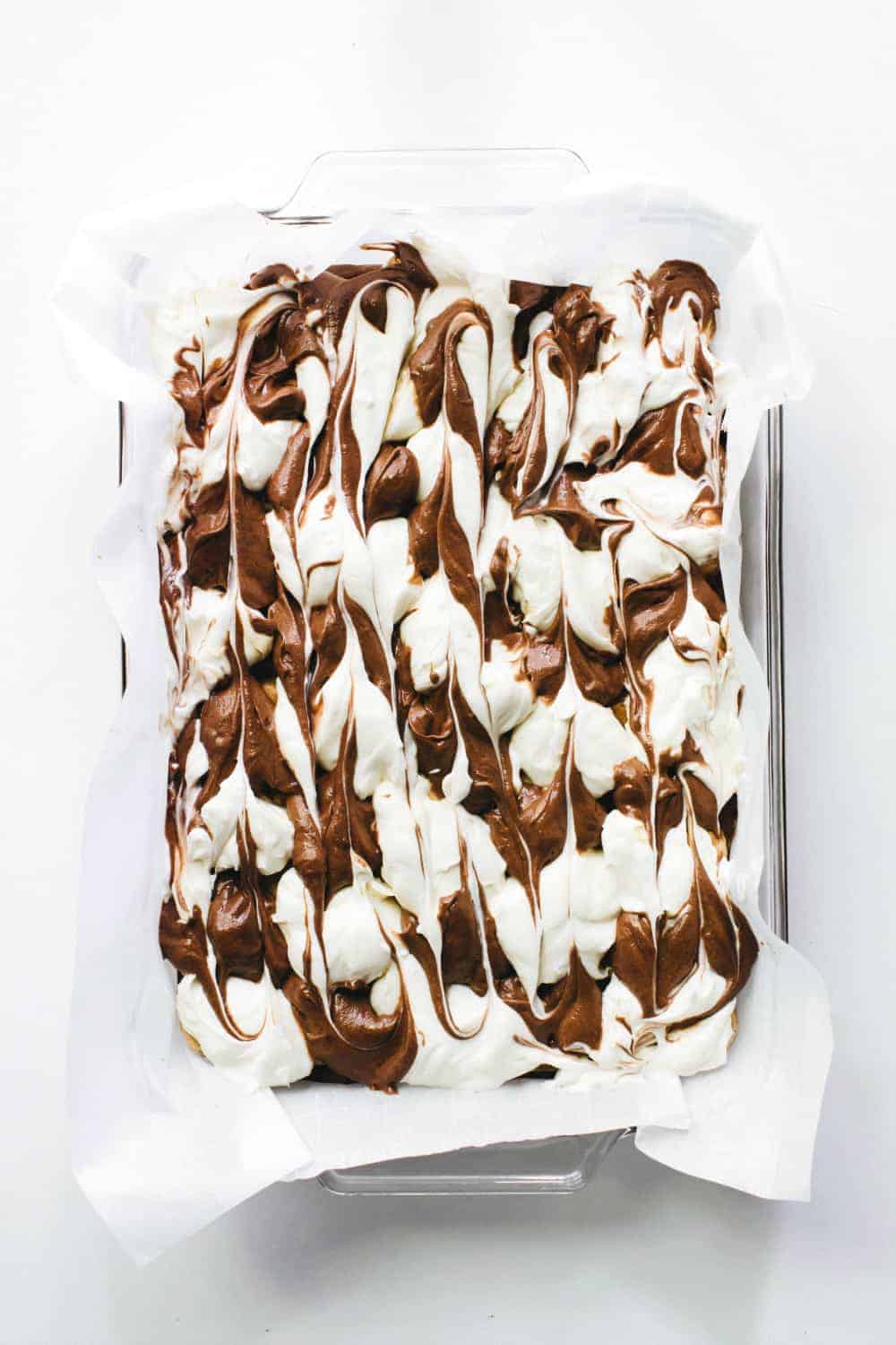 Overhead view of swirled brownie batter and mascarpone filling in a parchment-lined pan