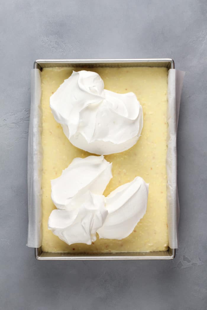 Cool Whip being added to the top of coconut cream bars in a metal pan.