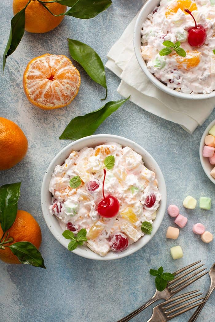 Two small white bowls of ambrosia salad, topped with maraschino cherries