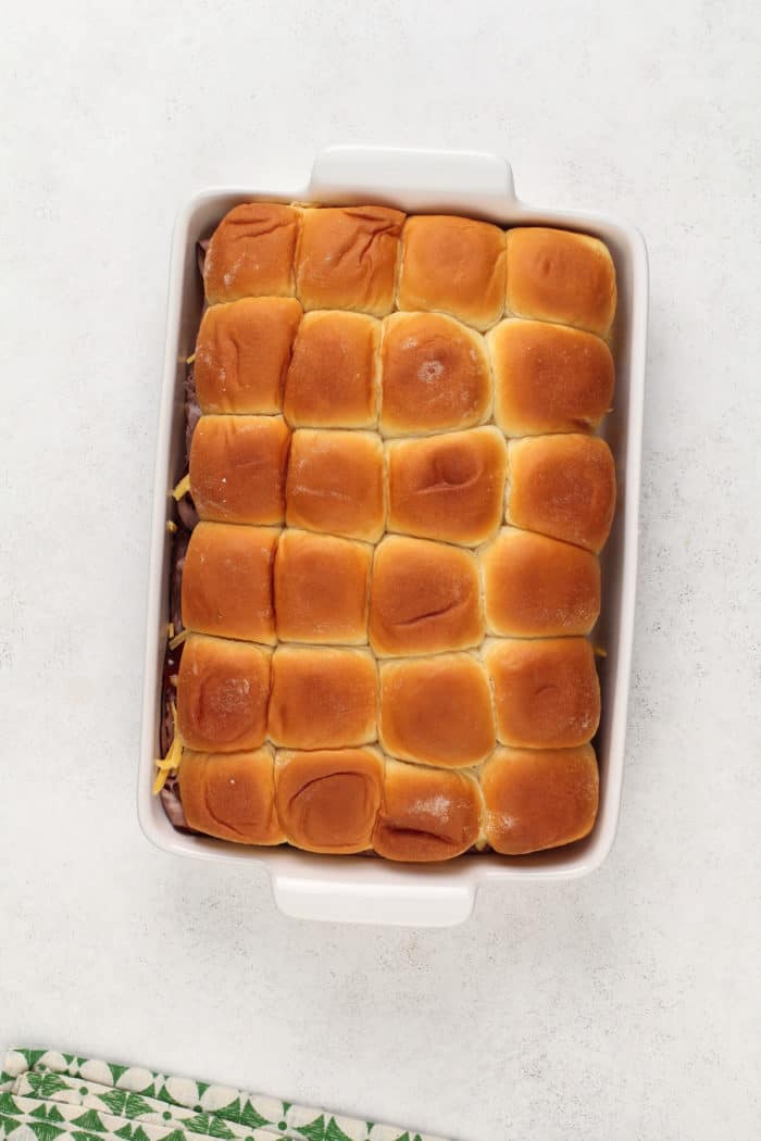 Unbaked cheesy roast beef sliders in a white baking dish.