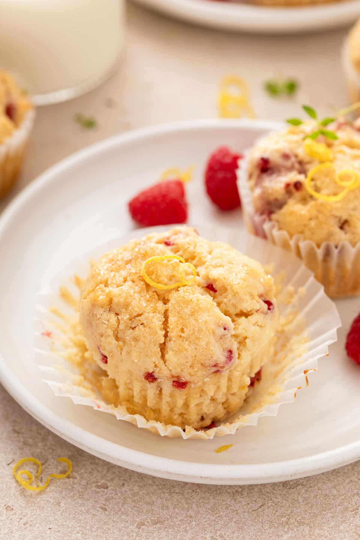 Two lemon raspberry muffins on a white plate. The muffin in front is unwrapped from its paper liner.