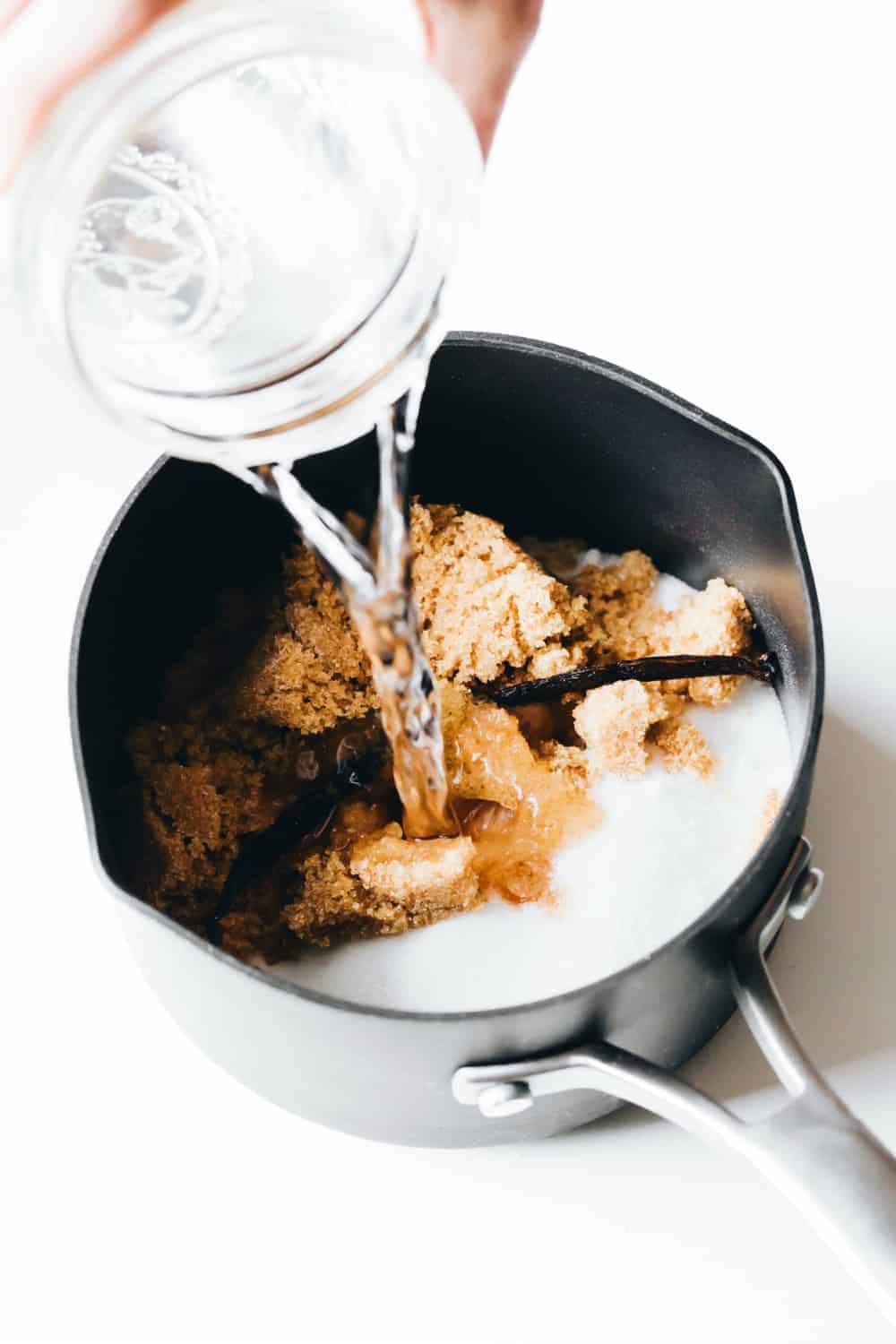 Jar adding water to a sauce pot with ingredients for vanilla coffee syrup