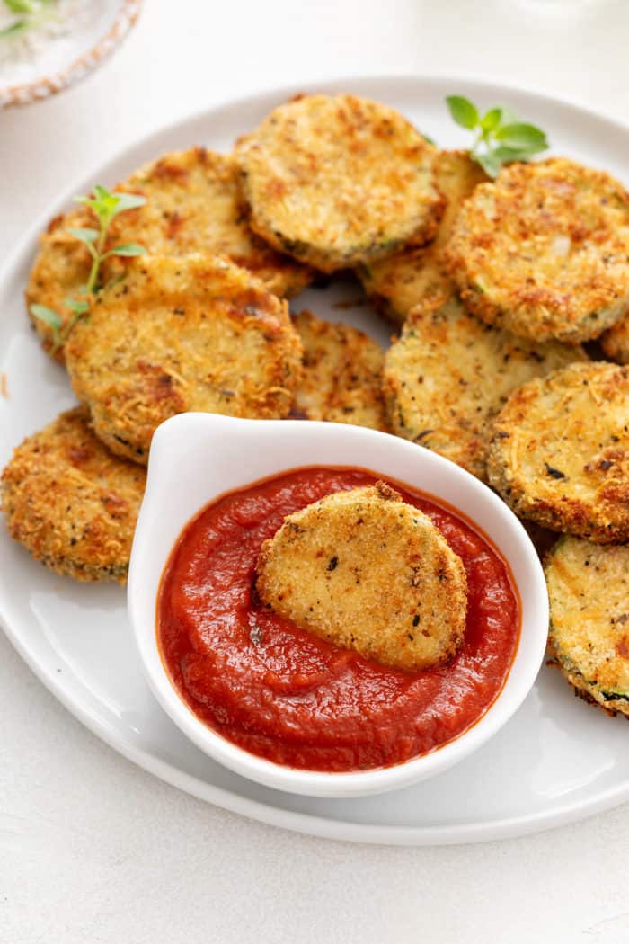 Air fryer zucchini chip in a small bowl of marinara sauce.