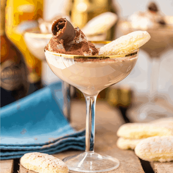 Side view of ladyfinger martini cocktail in a coupe glass on wood surface with blue napkin and ladyfinger cookies